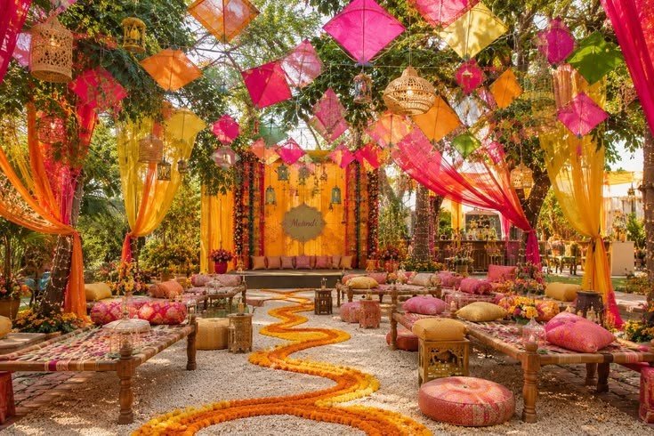 Boho mehendi decoration with macramé hangings, pampas grass, rattan seating, floor cushions, terracotta pots, and earthy floral accents.